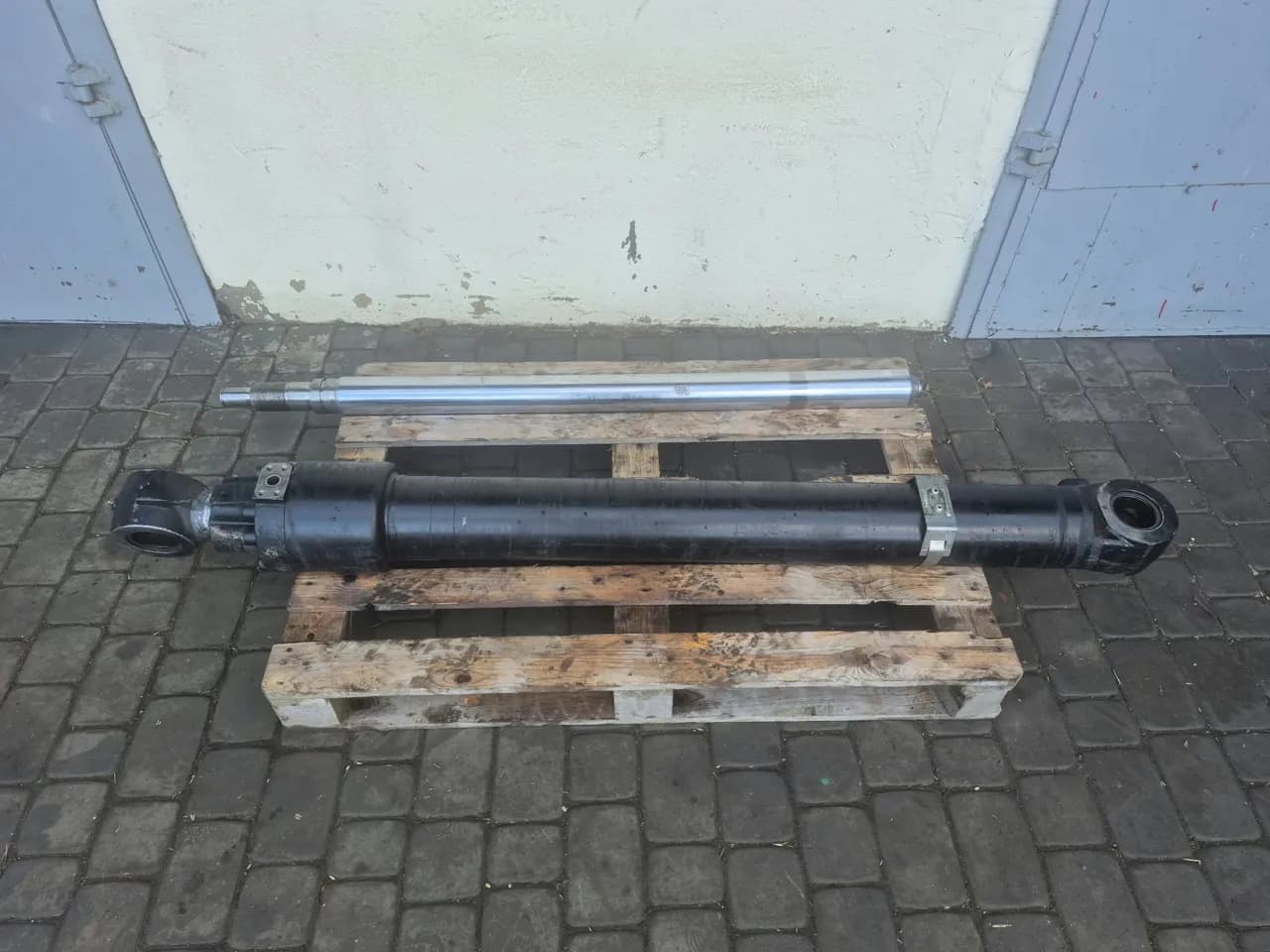 Długi czarny siłownik hydrauliczny i tłoczysko na palecie przed halą