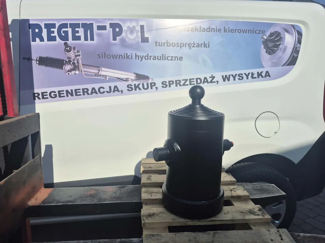 Teleskopowy siłownik wywrotu na palecie przed busem REGEN-POL z napisem „Regeneracja, skup, sprzedaż, wysyłka”