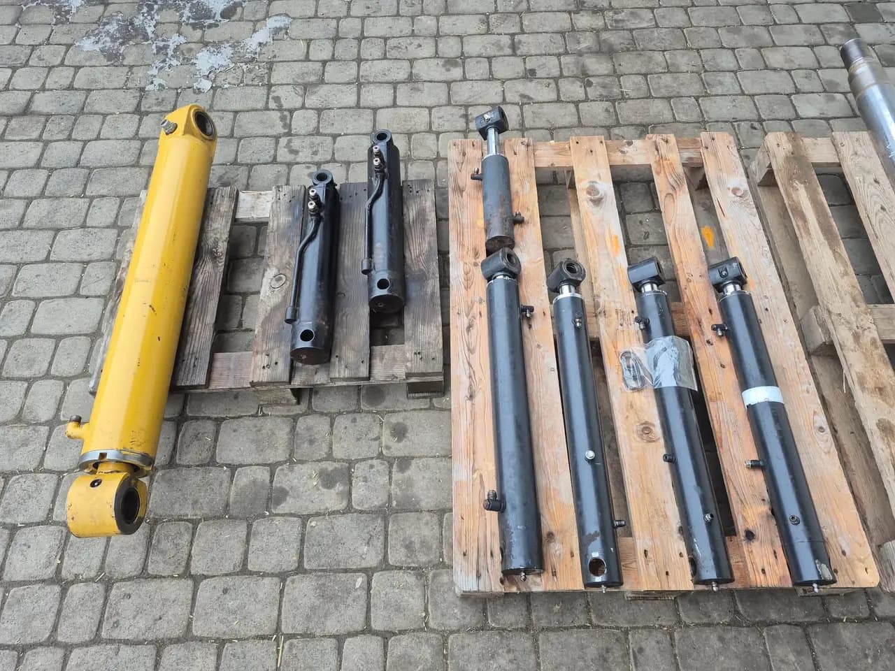 Siłowniki hydrauliczne różnych rozmiarów, żółty i czarne, ułożone na paletach