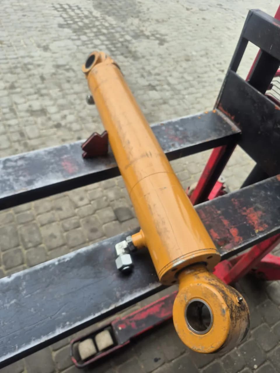 Żółty siłownik hydrauliczny z przewodem na widłach wózka paletowego